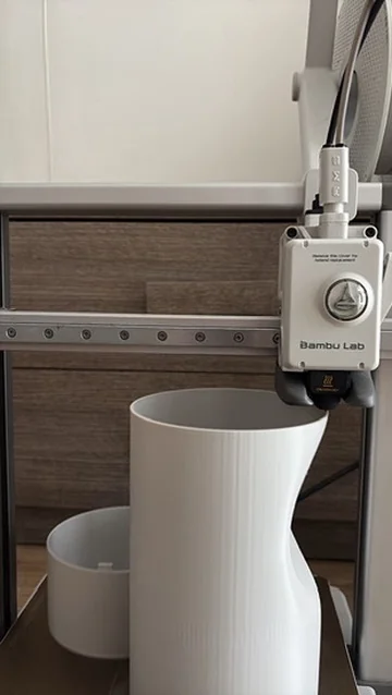 3D printer finishing a curved white vase form