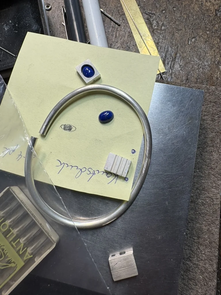 Silver bangle, lapis lazuli cabochons, and a small textured silver block laid out for the design