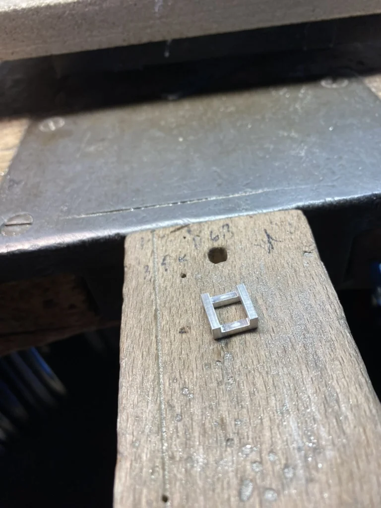 Small soldered silver bracket piece on a wooden bench pin