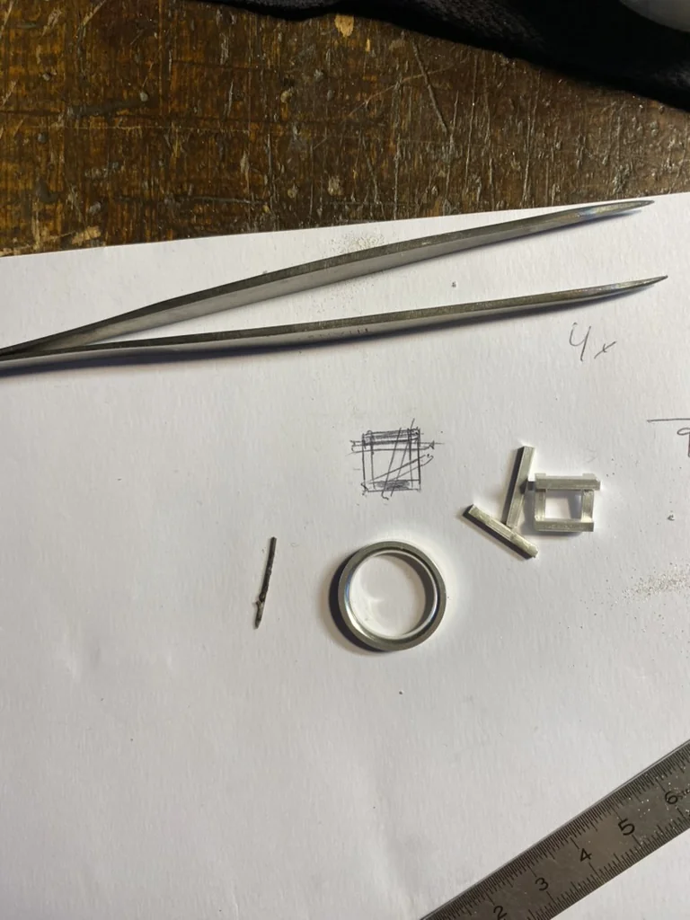 Ring band and geometric silver pieces laid out for assembly, next to a sketch