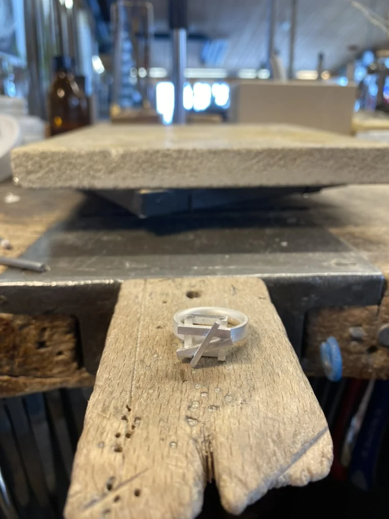 Finished silver ring with crossing geometric bars on the workbench