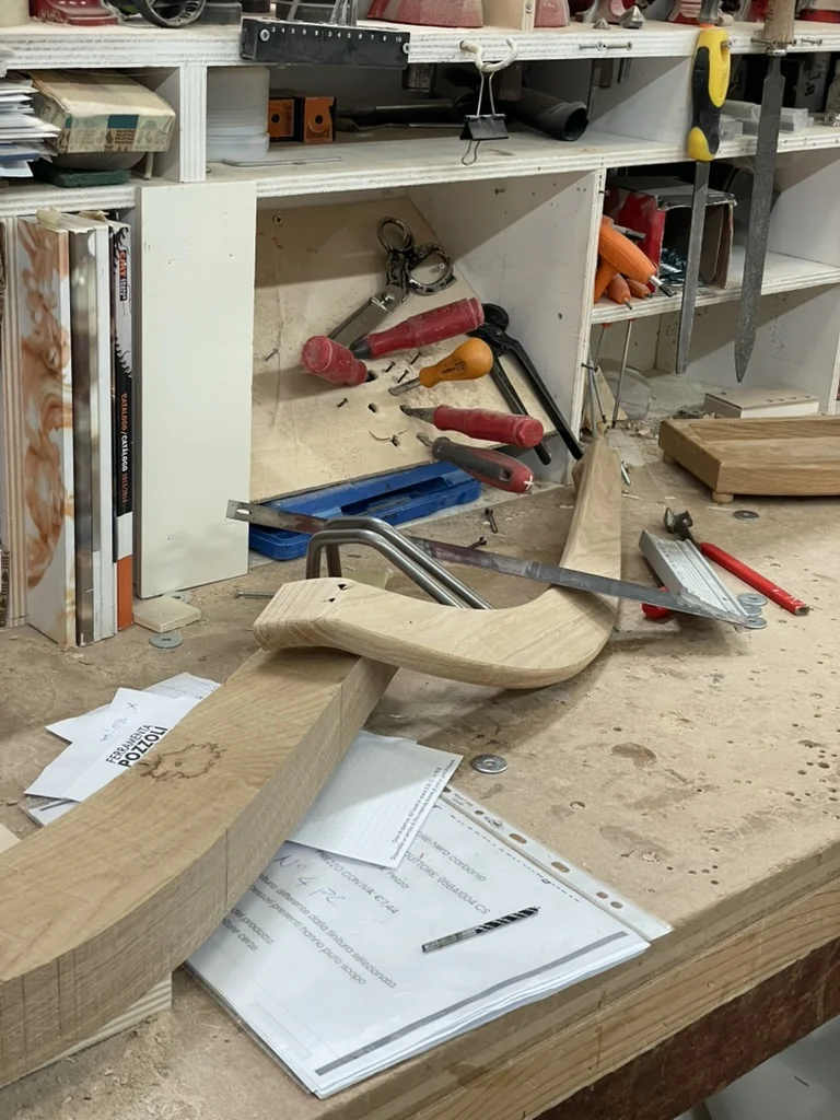 Wood leg pieces and hardware laid out on the workbench at Rivatelier