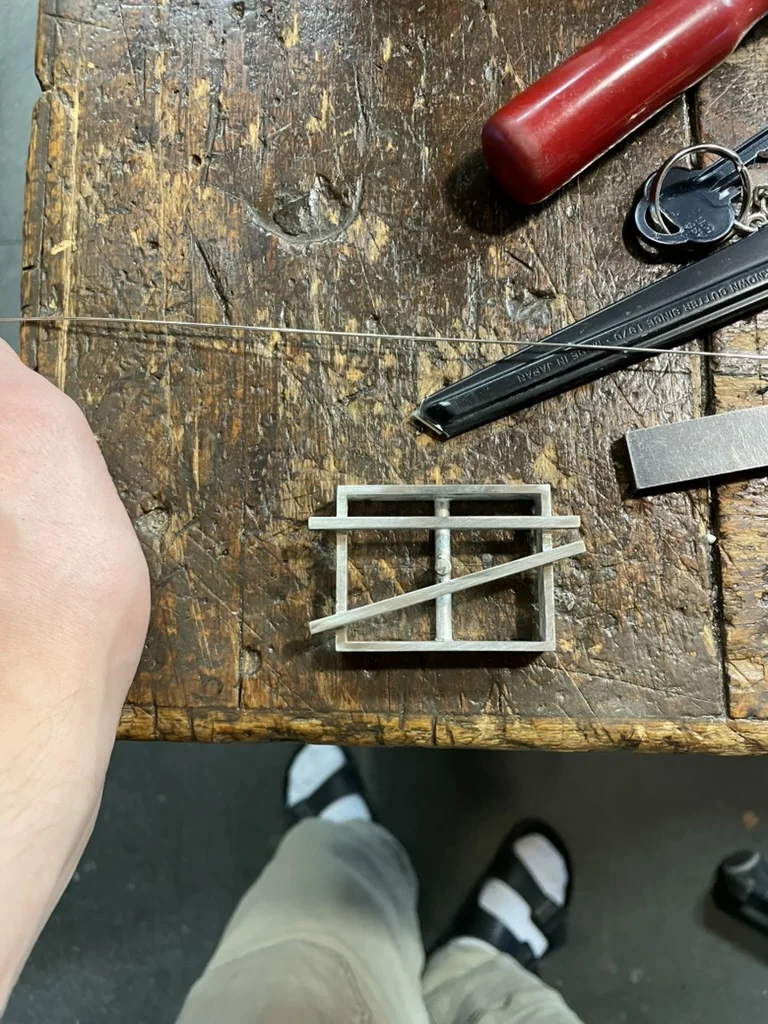 Silver buckle frame laid out on the workbench with saw wire and cutting tools